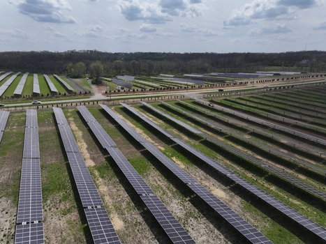 Lebanon United States 12 April 2026 Aerial view of a large solar farm with rows of photovoltaic panels a road with passing cars and a dense forest line under a cloudy sky.