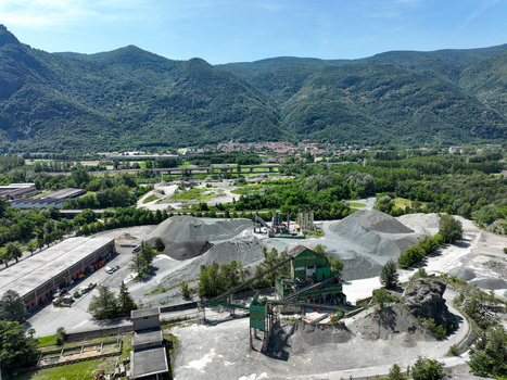 Aerial view of an industrial quarry with gravel piles and machinery nestled in a green valley against the backdrop of the Alps in Caprie Piedmont Italy. Aerial view of an industrial quarry with gravel piles and machinery nestled in a green valley against the backdrop of the Alps in Caprie Piedmont Italy.