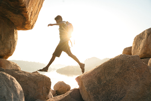 View of a man with a backpack jumping between large boulders during golden hour in Hampi Karnataka India. View of a man with a backpack jumping between large boulders during golden hour in Hampi Karnataka India.