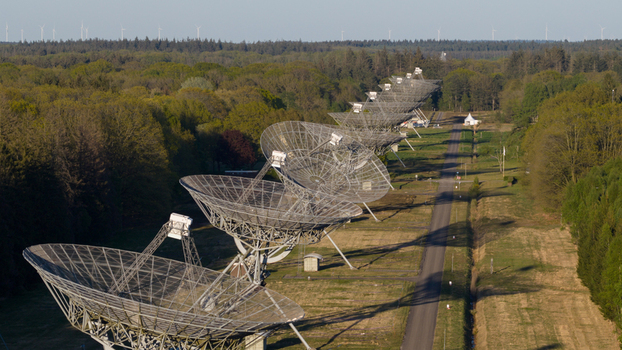 Aerial view of the Westerbork Synthesis Radio Telescope dishes lined up along a path surrounded by dense green forest and distant wind turbines in Westerbork Drenthe Netherlands. Aerial view of the Westerbork Synthesis Radio Telescope dishes lined up along a path surrounded by dense green forest and distant wind turbines in Westerbork Drenthe Netherlands.
