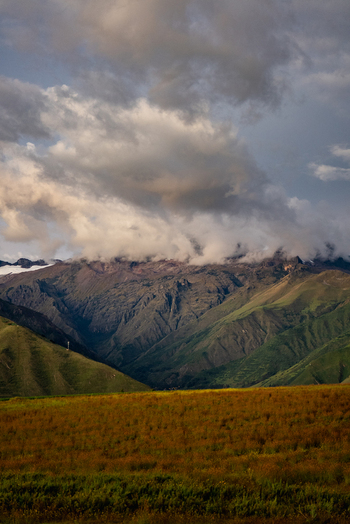 View of dramatic storm clouds gathering over the rugged mountains of the Sacred Valley at sunset with golden light illuminating the foreground fields in Urubamba Province Cusco Peru. View of dramatic storm clouds gathering over the rugged mountains of the Sacred Valley at sunset with golden light illuminating the foreground fields in Urubamba Province Cusco Peru.