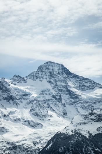 View of the crisp snow laden mountain peak rises against a backdrop of soft blue sky and wispy clouds a scene of serene alpine beauty Wengen Switzerland. View of the crisp snow laden mountain peak rises against a backdrop of soft blue sky and wispy clouds a scene of serene alpine beauty Wengen Switzerland.