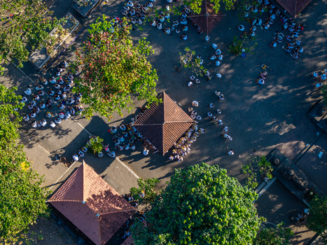 Aerial view of the Ngelarung Sea Offering Ceremony at Pura Segara Goa Lawah with people in traditional white clothing gathered around temple pavilions in Dawan Bali Indonesia.