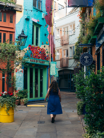 View of a lone figure strolling through a kaleidoscope of vivid teal crimson and white buildings in a charming verdant alleyway London England United Kingdom. View of a lone figure strolling through a kaleidoscope of vivid teal crimson and white buildings in a charming verdant alleyway London England United Kingdom.