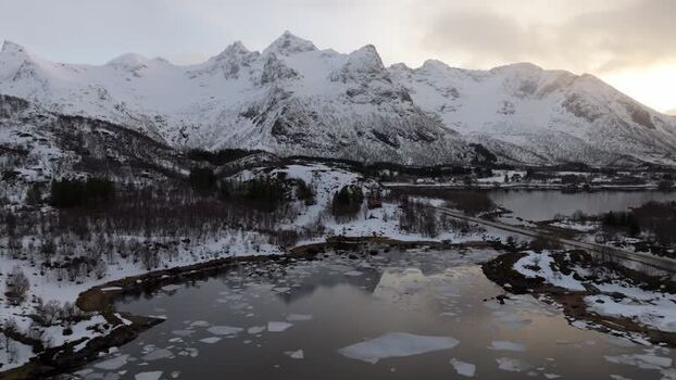 Aerial view of snow capped mountains and icy lake in Lofoten Norway.