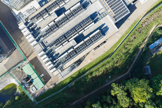 Aerial view of a data center with rooftop cooling units and solar panels surrounded by a fenced perimeter and green space in the United Kingdom.