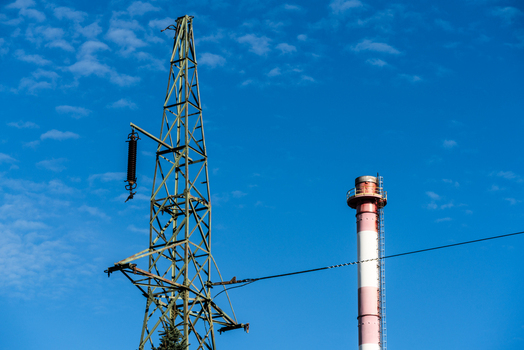 View of an electricity transmission pylon and a tall industrial chimney against a clear blue sky in Poland.
