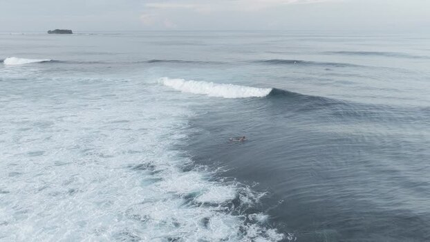Aerial view of a surfer paddling in waves in Siargao Philippines.