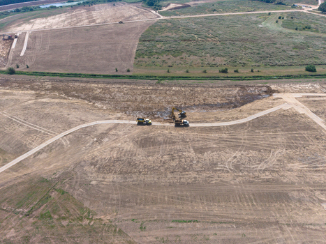 Aerial view of a construction site featuring an excavator and a dump truck working on a dirt road in a large cleared field in the Netherlands. Aerial view of a construction site featuring an excavator and a dump truck working on a dirt road in a large cleared field in the Netherlands.