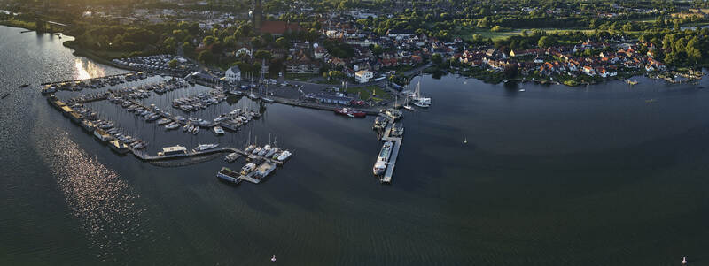 Schleswig Germany 01 July 2026 Aerial view of Schleswig Harbour on the Schlei featuring numerous boats docked at the marina historic town buildings and lush greenery at sunset.