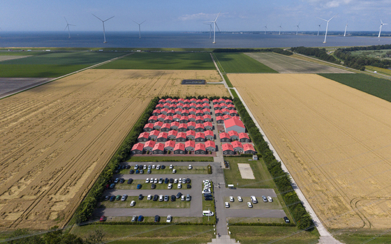 Aerial view of prefabricated housing for migrant and seasonal workers with red roofs surrounded by agricultural fields and wind turbines in Swifterbant Flevoland Netherlands. Aerial view of prefabricated housing for migrant and seasonal workers with red roofs surrounded by agricultural fields and wind turbines in Swifterbant Flevoland Netherlands.