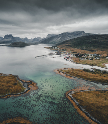 Aerial view of Flakstadbruene bridge spanning the turquoise waters of the fjord with a small village and rugged mountains under a cloudy sky in Flakstad Nordland Norway. Aerial view of Flakstadbruene bridge spanning the turquoise waters of the fjord with a small village and rugged mountains under a cloudy sky in Flakstad Nordland Norway.