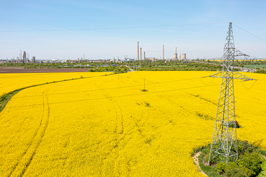 Aerial view of a blooming rapeseed field with an electricity pylon and an industrial complex under a clear blue sky Ploiesti Prahova Romania. Aerial view of a blooming rapeseed field with an electricity pylon and an industrial complex under a clear blue sky Ploiesti Prahova Romania.