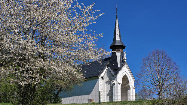 Aerial view of the Chapelle Notre Dame de Riantmont with a blossoming cherry tree under a clear blue sky in Vesancy Auvergne Rhone Alpes France. Aerial view of the Chapelle Notre Dame de Riantmont with a blossoming cherry tree under a clear blue sky in Vesancy Auvergne Rhone Alpes France.