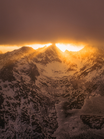 Aerial view of the snow capped peaks piercing through a golden sunrise casting long shadows across the rugged landscape Nordland Norway.