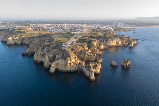 Aerial view of the dramatic limestone cliffs and rock formations at Ponta da Piedade with the town and coastline visible in the background in Lagos Faro District Portugal.