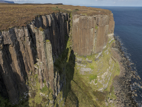 Aerial view of the dramatic basalt columns of Kilt Rock rising above the sea on the Isle of Skye with rugged grassy clifftops and deep shadows in Scotland United Kingdom. Aerial view of the dramatic basalt columns of Kilt Rock rising above the sea on the Isle of Skye with rugged grassy clifftops and deep shadows in Scotland United Kingdom.