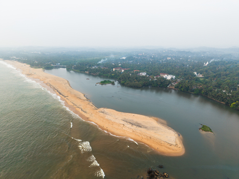 Aerial view of the sandy coastline and lush tropical greenery where the river meets the Indian Ocean under a hazy sky in Galle Southern Province Sri Lanka.