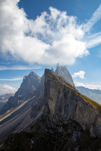 View of the jagged peaks of the Dolomites with steep rocky ridges and green alpine slopes under a blue sky with white clouds Rocca Pietore Veneto Italy. View of the jagged peaks of the Dolomites with steep rocky ridges and green alpine slopes under a blue sky with white clouds Rocca Pietore Veneto Italy.