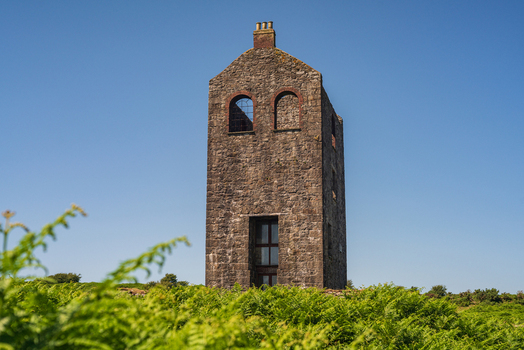View of the historic stone engine house at the former mining site surrounded by green ferns under a clear blue sky in Minions Cornwall United Kingdom. View of the historic stone engine house at the former mining site surrounded by green ferns under a clear blue sky in Minions Cornwall United Kingdom.