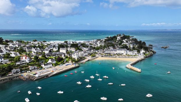 Aerial view of the coastal town of Locquirec with white houses a sandy beach and boats anchored in the turquoise harbor under a blue sky Locquirec Brittany France. Aerial view of the coastal town of Locquirec with white houses a sandy beach and boats anchored in the turquoise harbor under a blue sky Locquirec Brittany France.
