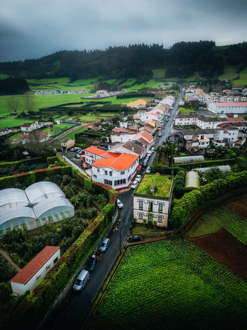 Aerial view of a quaint town nestled amidst rolling green hills where terracotta roofs meet lush fields under a soft overcast sky Furnas Azores Portugal.