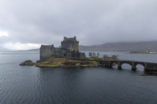 Aerial view of Eilean Donan Castle on its tidal island with the stone bridge and misty mountains under a cloudy sky Dornie Scotland United Kingdom.