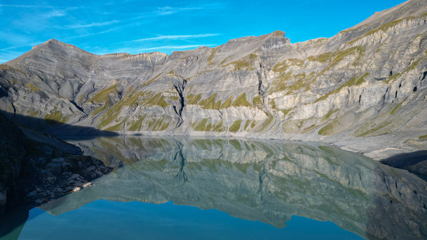 Aerial view of the serene Vieux Emosson Lake reflecting the surrounding rugged mountain peaks and rocky slopes under a clear blue sky in Finhaut Valais Switzerland. Aerial view of the serene Vieux Emosson Lake reflecting the surrounding rugged mountain peaks and rocky slopes under a clear blue sky in Finhaut Valais Switzerland.