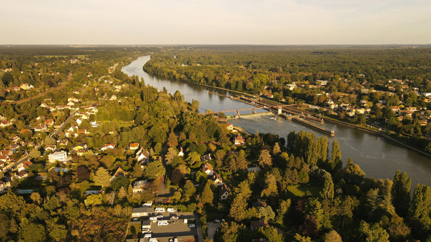 Aerial view of the Seine river flowing through the town featuring a lock system lush forests and residential houses under warm golden hour light in Chartrettes Ile de France France. Aerial view of the Seine river flowing through the town featuring a lock system lush forests and residential houses under warm golden hour light in Chartrettes Ile de France France.