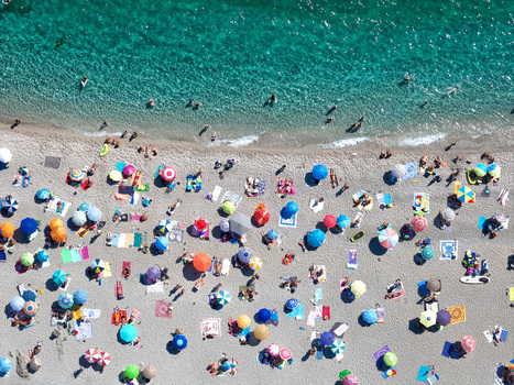 Aerial view of a public beach with colorful umbrellas sunbathers relaxing on the sand and clear turquoise water along the coastline in Bergeggi Liguria Italy.