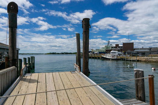 View of Martha s Vineyard harbor with a wooden ferry ramp pilings and boats under a cloudy blue sky Edgartown Massachusetts United States.