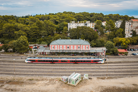 Aerial view of a modern train stopped at the historic Buzet railway station surrounded by lush green trees and urban infrastructure in Buzet Istria County Croatia.