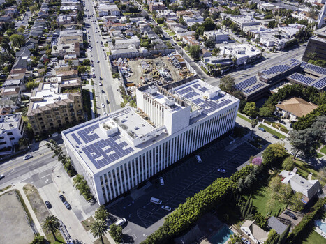 Aerial view of a modern office building featuring rooftop photovoltaic solar panel arrays and HVAC units surrounded by urban streets in Los Angeles California United States. Aerial view of a modern office building featuring rooftop photovoltaic solar panel arrays and HVAC units surrounded by urban streets in Los Angeles California United States.