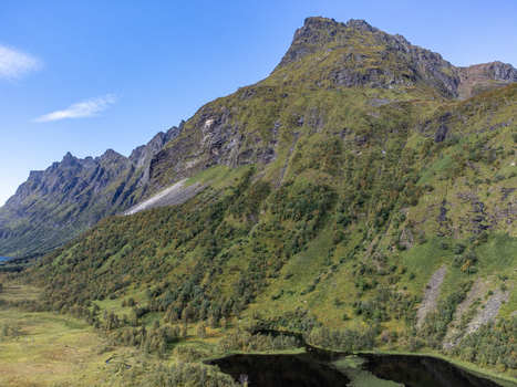 Aerial view of verdant slopes meet jagged peaks under a vast sky whispering tales of ancient landscapes M&oslash;ysalen Nordland Norway.