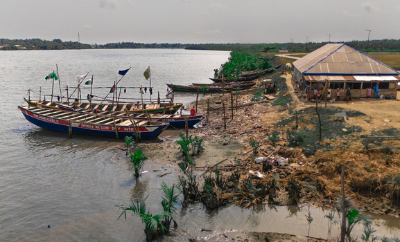 Aerial view of wooden fishing boats moored along the riverbank near a small building with people standing nearby in Minima Rivers Nigeria.