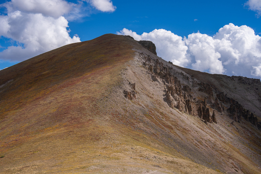 View of the rugged slopes and rocky formations of San Luis Peak under a bright blue sky with scattered clouds in Creede Colorado United States. View of the rugged slopes and rocky formations of San Luis Peak under a bright blue sky with scattered clouds in Creede Colorado United States.