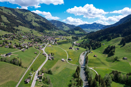 Aerial view of the village of Rougemont nestled in a lush green valley with a winding river and forested mountains under a blue sky Rougemont Vaud Switzerland. Aerial view of the village of Rougemont nestled in a lush green valley with a winding river and forested mountains under a blue sky Rougemont Vaud Switzerland.