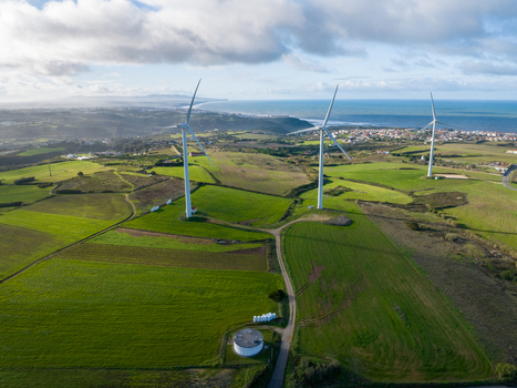 Aerial view of wind turbines standing on lush green hills overlooking the Atlantic coast under a cloudy sky Ribamar Portugal. Aerial view of wind turbines standing on lush green hills overlooking the Atlantic coast under a cloudy sky Ribamar Portugal.