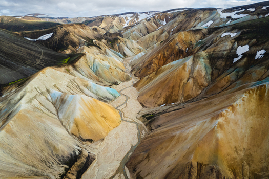Aerial view of Landmannalaugar rhyolite mountains with colorful slopes winding riverbed and snow patches in Rangarthing ytra Iceland. Aerial view of Landmannalaugar rhyolite mountains with colorful slopes winding riverbed and snow patches in Rangarthing ytra Iceland.