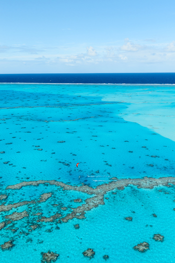 Aerial view of Aitutaki lagoon with vibrant turquoise waters coral reefs and a kite surfer gliding across the surface in the Cook Islands. Aerial view of Aitutaki lagoon with vibrant turquoise waters coral reefs and a kite surfer gliding across the surface in the Cook Islands.