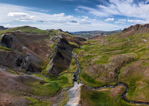 Aerial view of Grensdalur valley with a winding stream geothermal steam vents and vibrant green hills under a blue sky in Sveitarfelagid Olfus Iceland. Aerial view of Grensdalur valley with a winding stream geothermal steam vents and vibrant green hills under a blue sky in Sveitarfelagid Olfus Iceland.