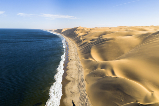 Aerial view of the shoreline where the deep blue ocean meets the towering rolling dunes of the desert creating a stark contrast of color and texture Anichab Erongo Namibia. Aerial view of the shoreline where the deep blue ocean meets the towering rolling dunes of the desert creating a stark contrast of color and texture Anichab Erongo Namibia.