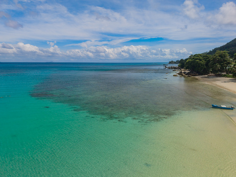 Aerial view of the turquoise ocean kissing the sandy shore near lush greenery a small boat resting peacefully on the beach Victoria Seychelles. Aerial view of the turquoise ocean kissing the sandy shore near lush greenery a small boat resting peacefully on the beach Victoria Seychelles.