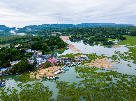 Aerial view of the lakeside settlement in Rangamati with wooden boats moored at the dock surrounded by lush green trees and rolling hills in Rangamati Chittagong Division Bangladesh. Aerial view of the lakeside settlement in Rangamati with wooden boats moored at the dock surrounded by lush green trees and rolling hills in Rangamati Chittagong Division Bangladesh.