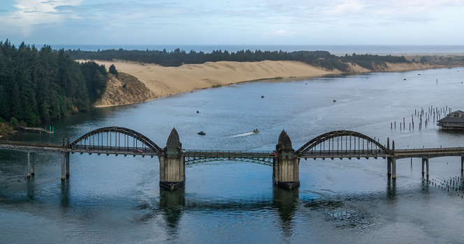 Aerial view of the Siuslaw River Bridge in Florence Oregon with salmon fishing boats on the river sand dunes and forest along the Oregon Coast. Aerial view of the Siuslaw River Bridge in Florence Oregon with salmon fishing boats on the river sand dunes and forest along the Oregon Coast.
