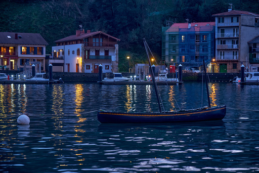 Pasai Donibane Spain 09 March 2026 View of a traditional wooden boat moored in the harbor along the historic waterfront buildings and coastal street at dusk.