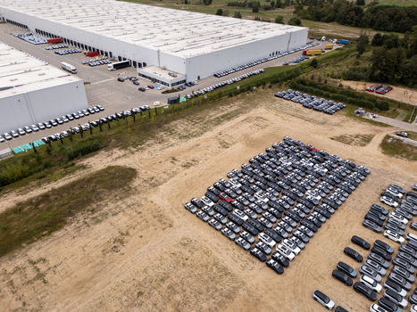 Aerial view of a large industrial warehouse facility with extensive parking lots filled with numerous new cars in Gdansk Poland. Aerial view of a large industrial warehouse facility with extensive parking lots filled with numerous new cars in Gdansk Poland.