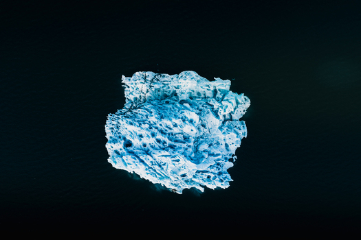 Aerial view of a bright blue iceberg floating in the dark waters of the Jokulsarlon glacier lagoon in Hornafjordur Iceland. Aerial view of a bright blue iceberg floating in the dark waters of the Jokulsarlon glacier lagoon in Hornafjordur Iceland.