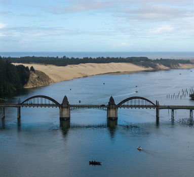 Aerial view of the Siuslaw River Bridge spanning the river with sand dunes in the background and small fishing boats on the water in Florence Oregon United States. Aerial view of the Siuslaw River Bridge spanning the river with sand dunes in the background and small fishing boats on the water in Florence Oregon United States.