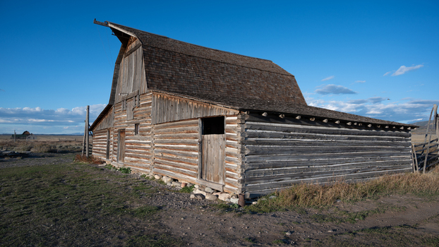 View of the historic wooden barn in Jackson Hole featuring weathered timber walls and a shingled roof under a clear blue sky in Teton County Wyoming United States.